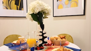 Una mesa de comedor con alimentos para el desayuno, una obra de arte enmarcada y un jarrón con flores.