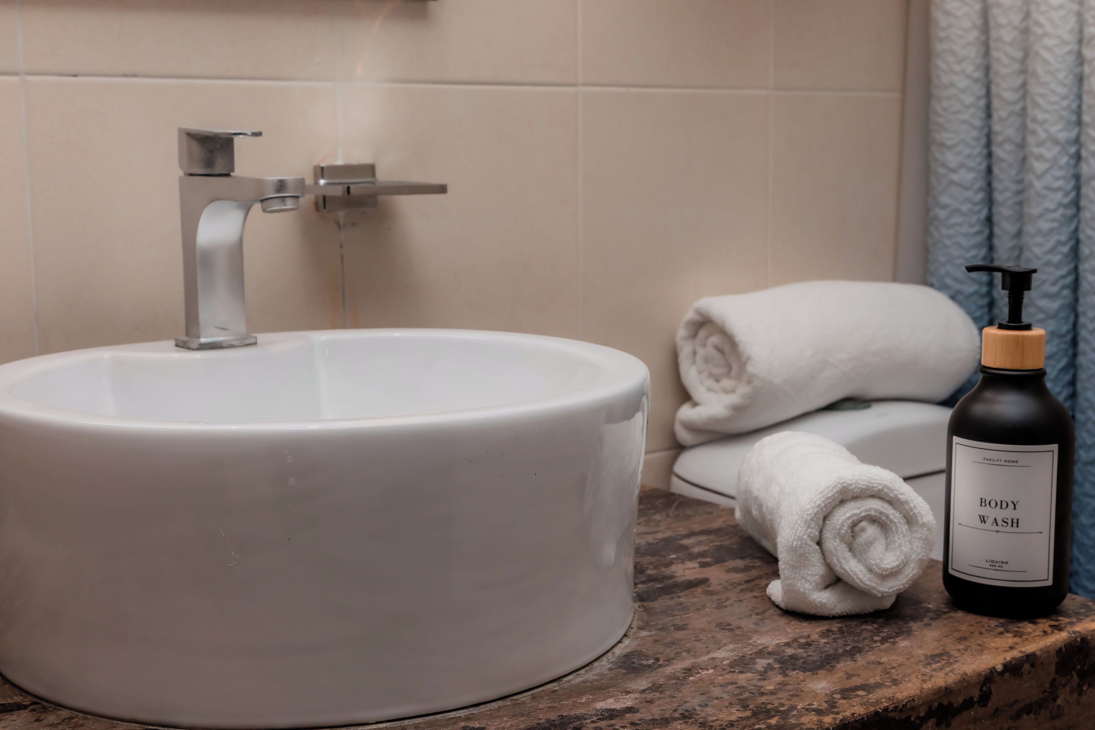 Une salle de bain avec un lavabo blanc, une serviette et un flacon de gel douche.