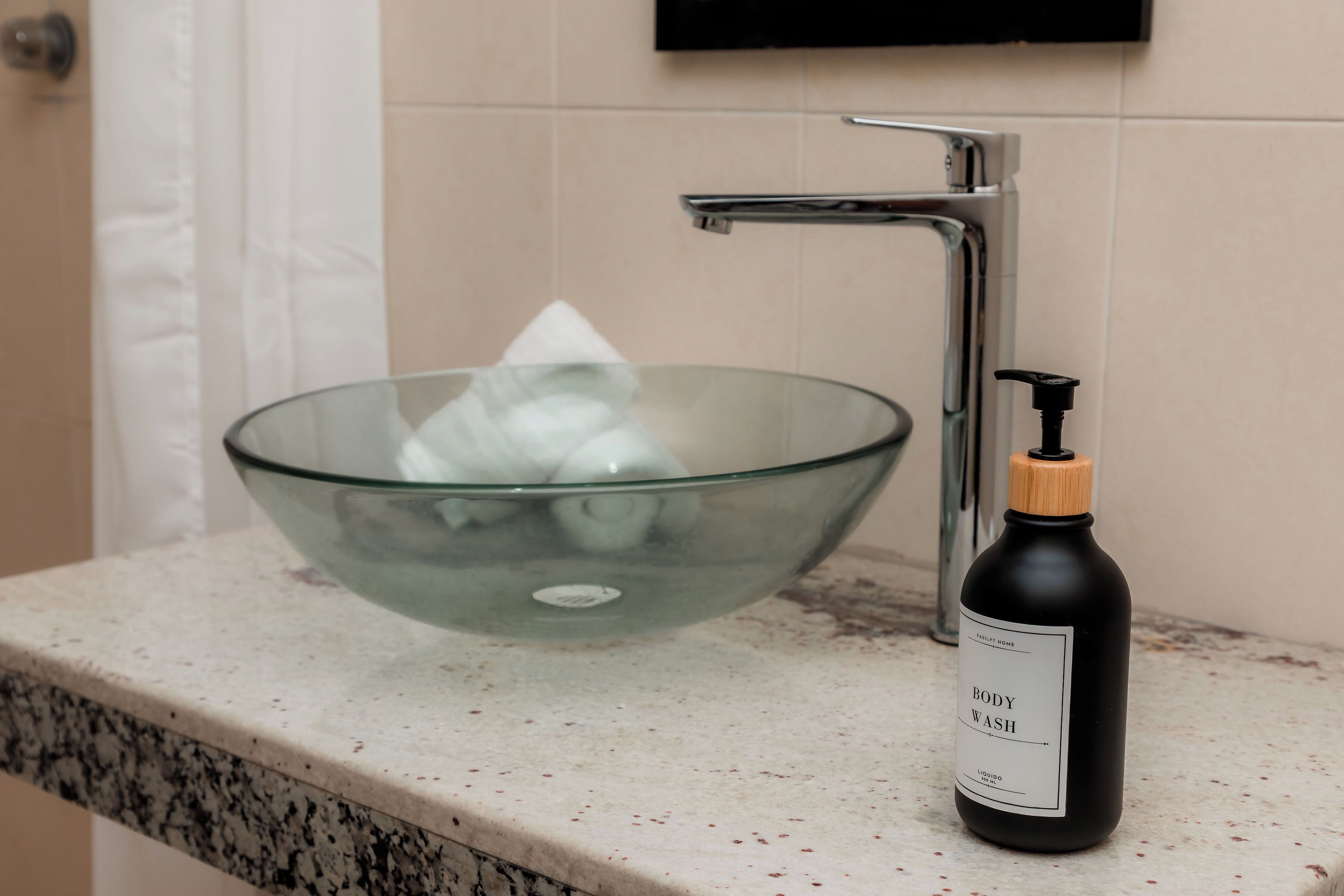 A bathroom with a glass bowl sink, a black bottle of body wash, and a chrome faucet.