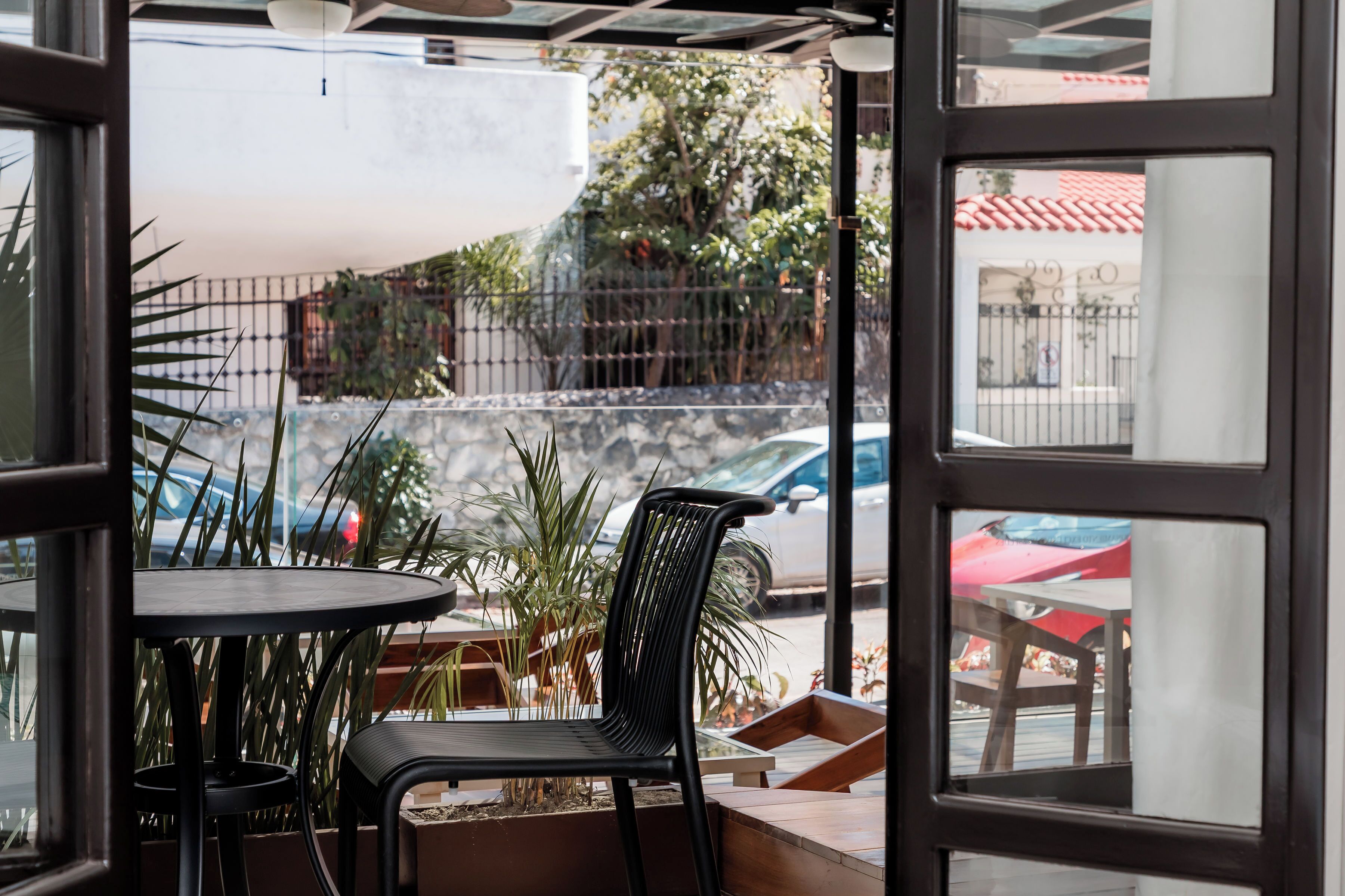 An outdoor seating area with a table and chairs, a potted plant, and a view of the street and buildings.