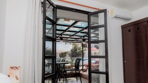 Une chambre avec un lit, une fenêtre donnant sur la rue, une table avec des chaises et un appareil de climatisation.
