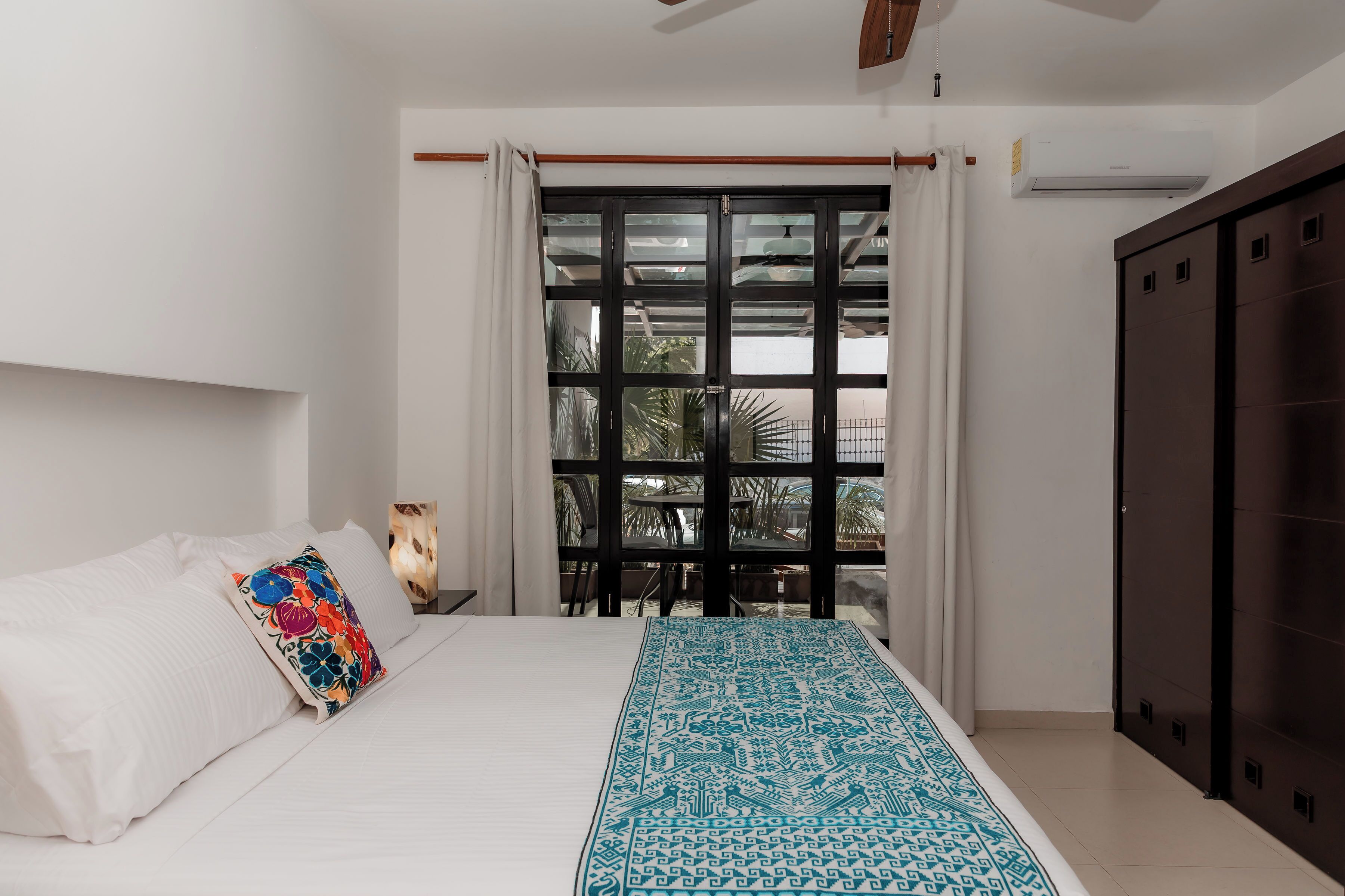 A bedroom with a bed, a window with curtains, a wardrobe, and an air conditioning unit.