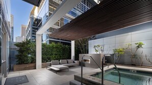 Ett modernt utomhuspoolområde med en träpergola, sittplatser och utsikt över de omgivande byggnaderna.