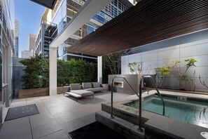 Uma área moderna com piscina ao ar livre, pérgola de madeira, assentos e vista para edifícios próximos.