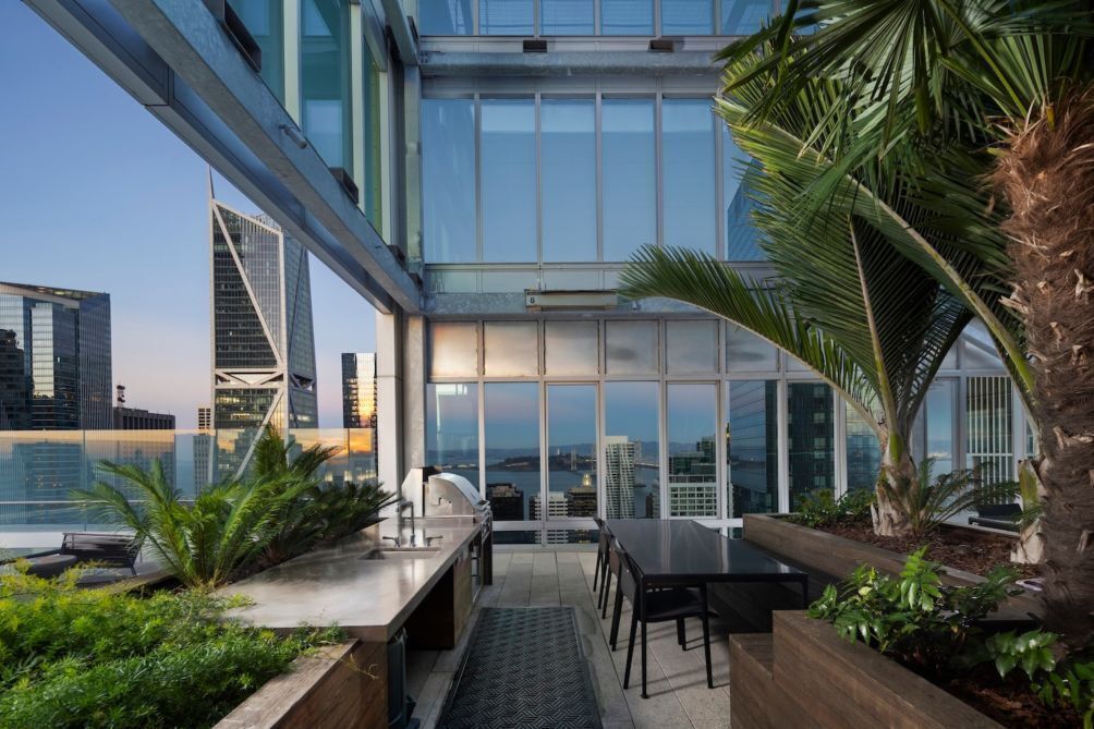 A modern rooftop terrace with a dining area, kitchen, and large windows offering city views.