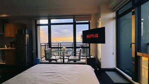 A hotel room with a bed, a TV mounted on the wall, a balcony with a city view, and a kitchenette. - Executive Studio w/ Sunset View - Makati CBD (Makati)