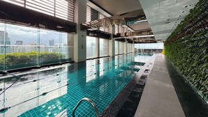 A modern indoor swimming pool with clear glass walls, a tiled floor, and a view of the cityscape. - Executive Studio w/ Sunset View - Makati CBD (Makati)