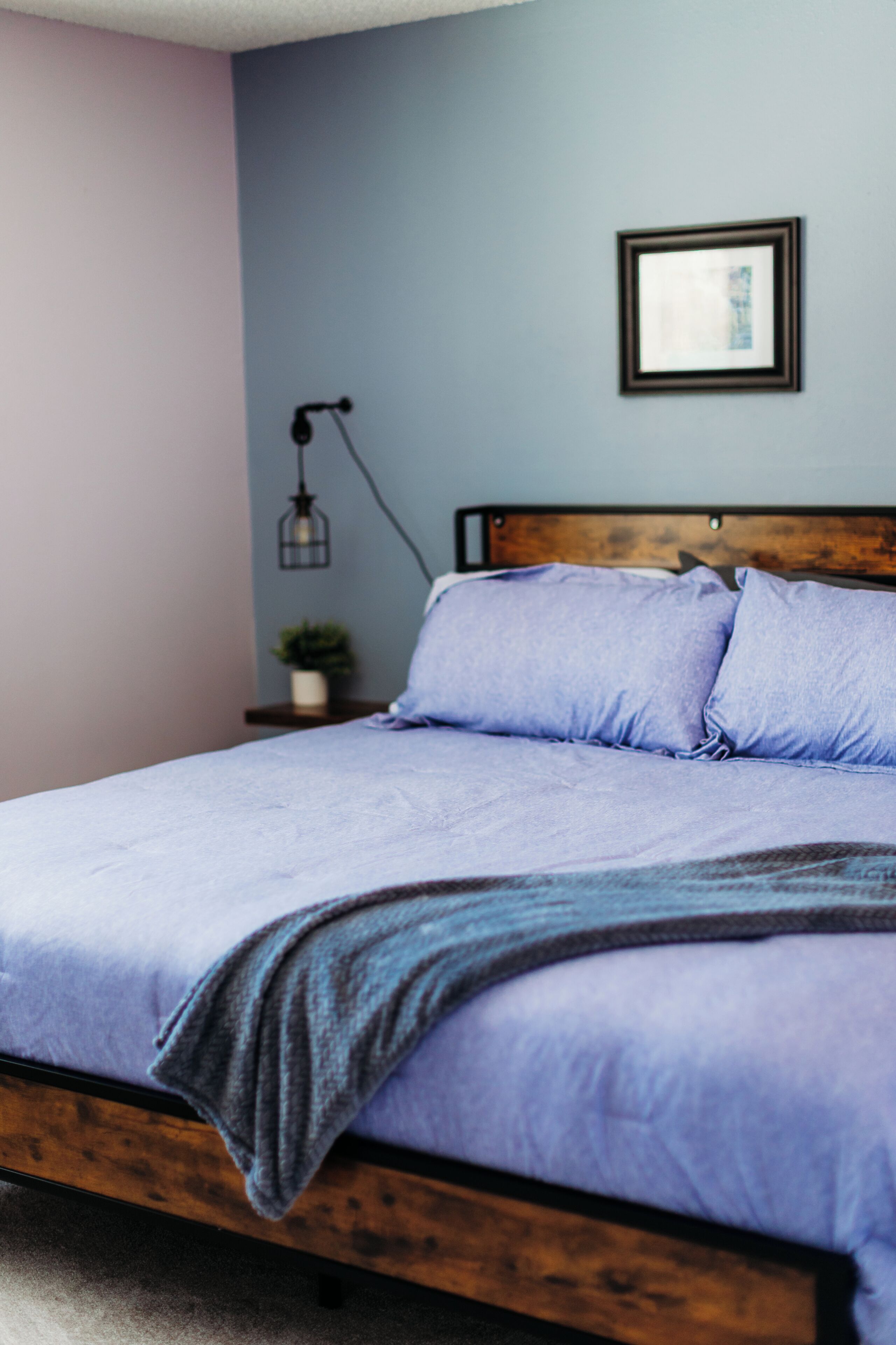 Un letto con struttura in legno, una testata blu e una abat-jour.