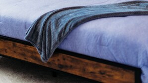 Ein Bett mit Holzrahmen, einem blauen Kopfteil und einer einzelnen Nachttischlampe.