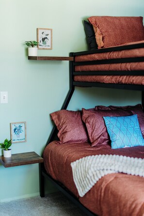 A bunk bed with a brown mattress and pillows, a small white plant on a shelf, and a framed picture on the wall.