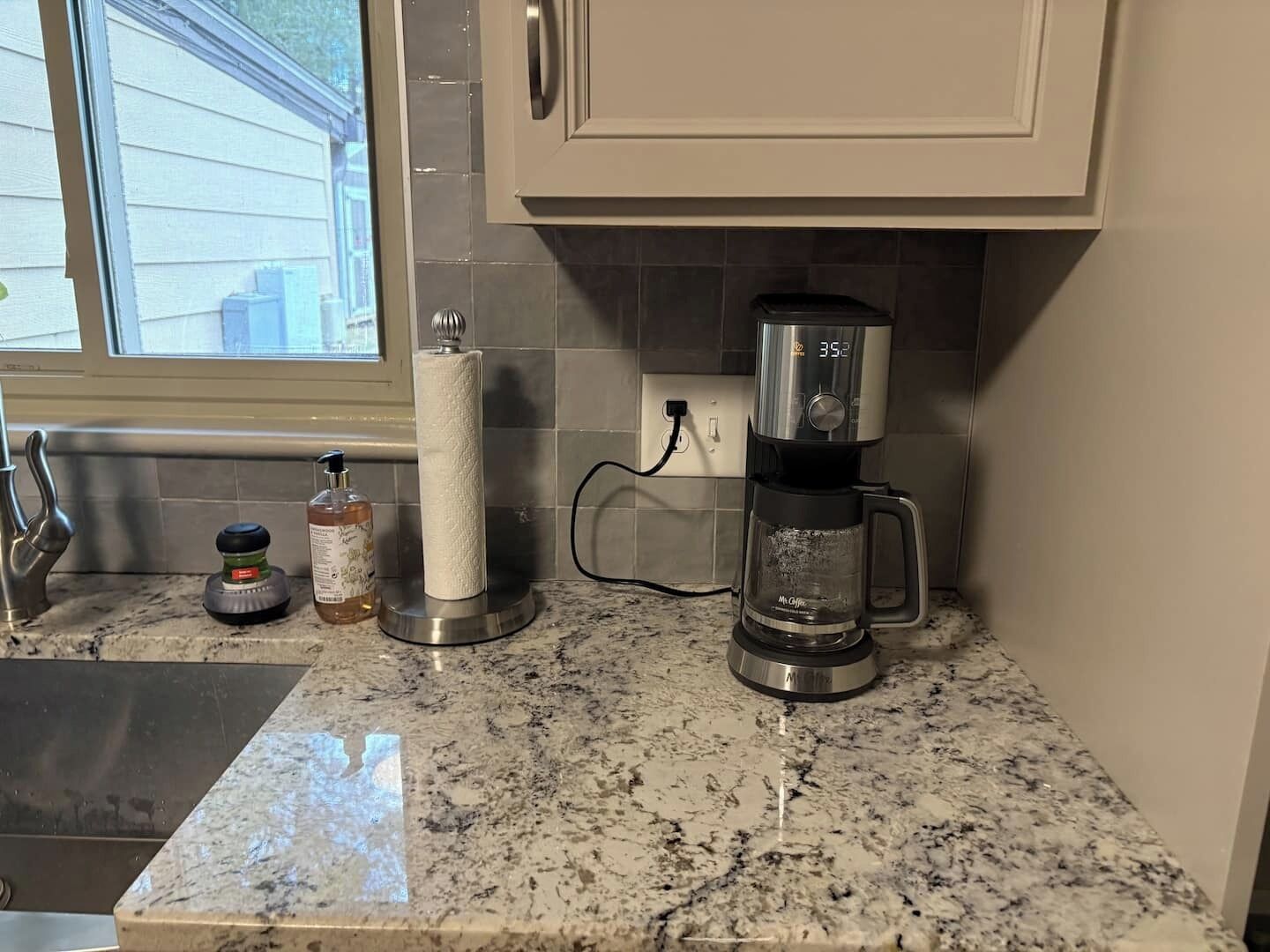 Een keuken met een koffiezetapparaat, een rek voor keukenpapier, een zeepdispenser en een fles handzeep.
