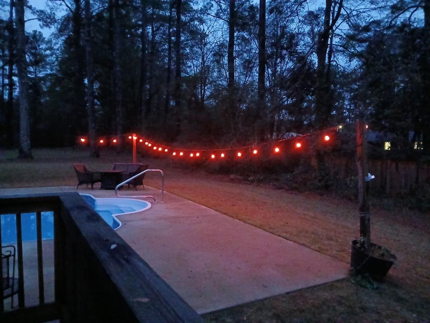A backyard with a pool, deck chairs, and string lights.
