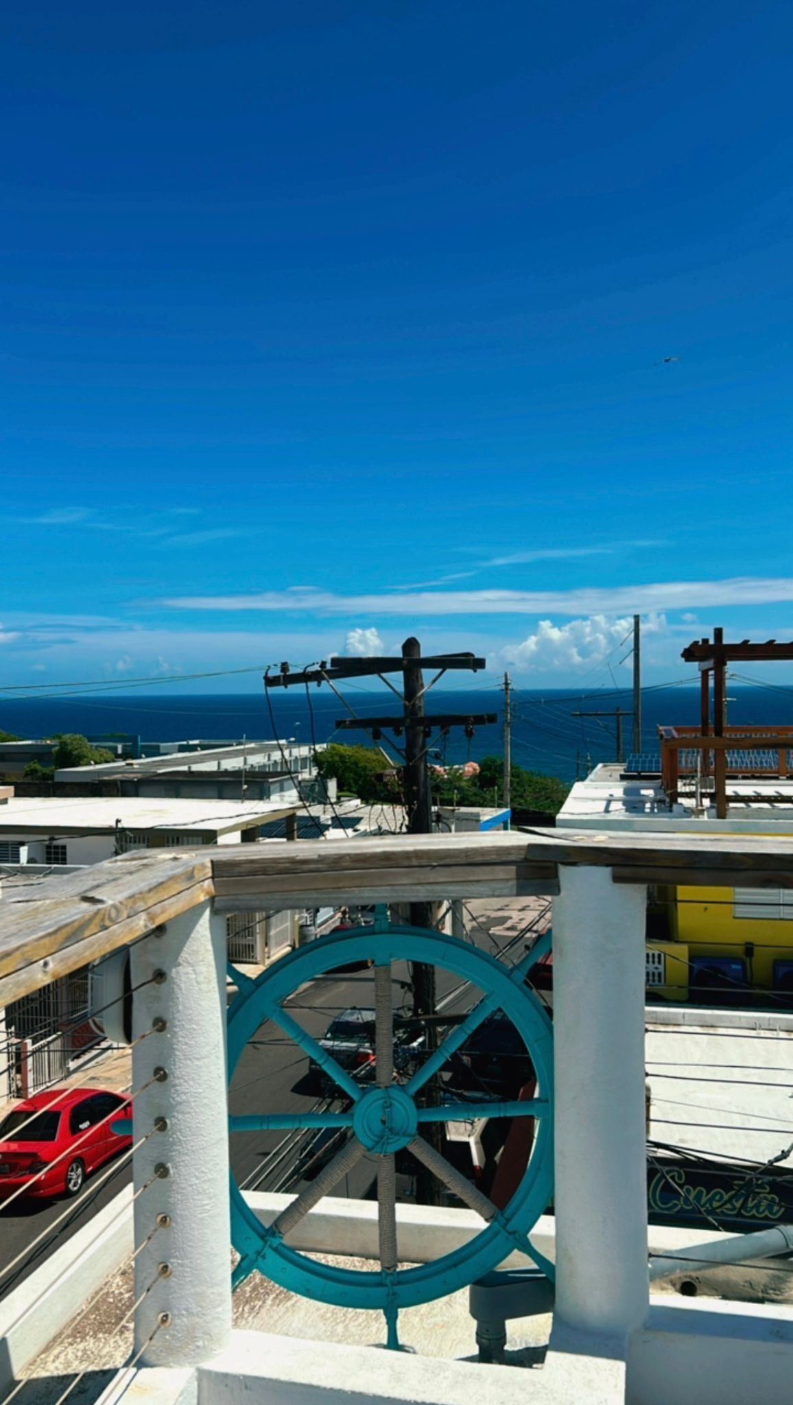 A rooftop with a large turquoise wheel, power lines, and a view of the ocean.