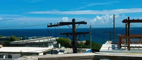 A rooftop with a large turquoise wheel, power lines, and a view of the ocean.