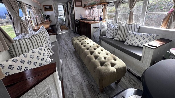 A cozy RV interior with a sofa, ottoman, and a small kitchen area. - Adorable 1-bedroom studio bus in charming Wears Valley (Sevierville)
