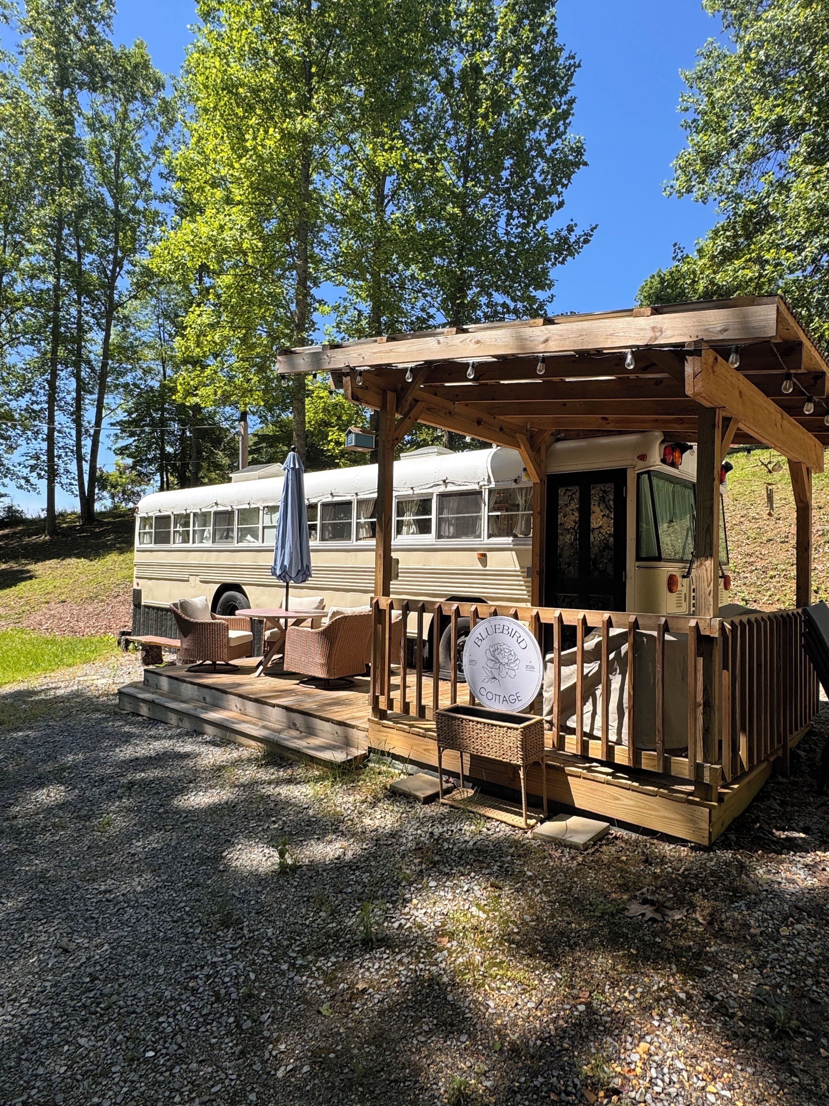 A rustic wooden structure with a porch, a vintage bus, and a sign reading 'Bluebird Cottage.'