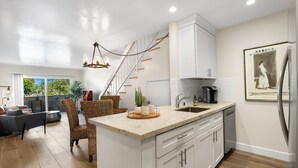 Une cuisine moderne avec des meubles blancs, un îlot central et un coin repas doté de chaises en osier.