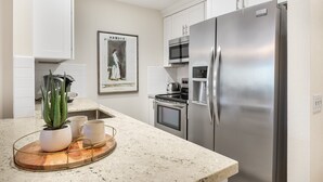 Une cuisine avec des meubles blancs, des appareils en acier inoxydable, un plan de travail en granit et un pot contenant une plante d’aloès.