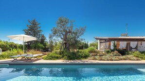 A swimming pool with lounge chairs and an umbrella, surrounded by greenery and a building with a tiled roof. - Room with shared pool in Salento countryside (Salve)