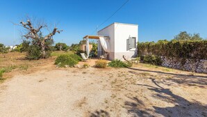 A single-story house with a white exterior, a small porch with a white awning, and a stone wall in the background. - Room with shared pool in Salento countryside (Salve)