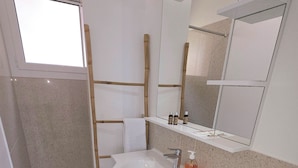 Un bagno con lavandino bianco, specchio e doccia. Sul lavandino sono presenti articoli da toilette e un porta asciugamani.