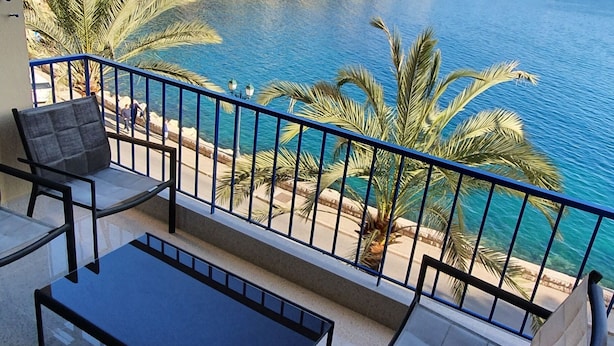 Un balcone con vista su un corpo d'acqua, una sedia, un tavolino e una ringhiera.