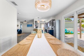 A modern kitchen with a central island, a dining area with a long table, and a view of the outdoor patio area. - Tiki Paradise Resort Heated Saltwater Pool (Largo)