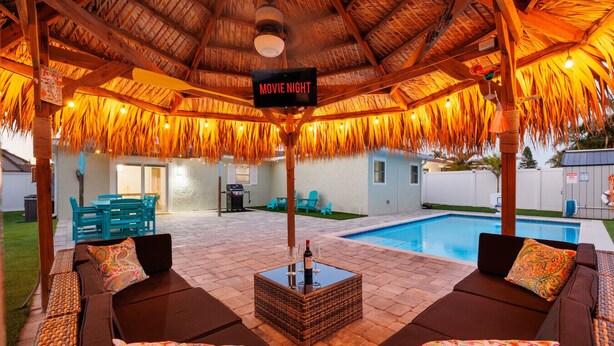 Patio esterno con piscina, un cartello che annuncia una serata cinema e un'area salotto coperta con cuscini.