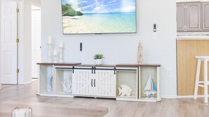 Un soggiorno con una TV montata a parete, un mobiletto bianco con anta in vetro e una piccola pianta sopra il mobiletto.