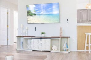 A living room with a TV mounted on the wall, a white cabinet with a glass door, and a small plant on the cabinet. - Tiki Paradise Resort Heated Saltwater Pool (Largo)