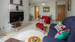 A living room with a TV, sofa, and dining area. - Apartamento com 3 Quartos e Garagem no Setor Bueno (Goiânia)