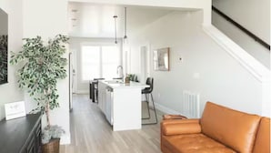 Uma sala de estar moderna com sofá de couro, área de jantar com ilha branca e cozinha com ilha central.