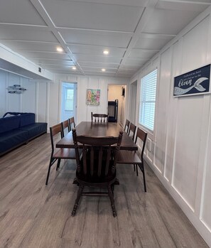 A dining area with a wooden table surrounded by chairs, a blue sofa, and a wall with a nautical-themed sign. - Marvelous 7-bedroom house in North Myrtle Beach Cherry Grove 2nd Row (North Myrtle Beach)