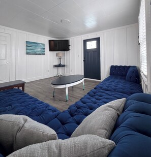 A room with a large bed, a small table, a television, and a door with a window. - Marvelous 7-bedroom house in North Myrtle Beach Cherry Grove 2nd Row (North Myrtle Beach)