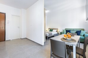Une chambre d’hôtel moderne avec un coin repas, un canapé vert et un lit avec une literie blanche.