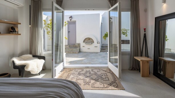 A modern bedroom with a large bed, a chair, a small table, and a view of the outside. - Yema House - Naoussa Bay (4666+369 Protorgia, Greece)