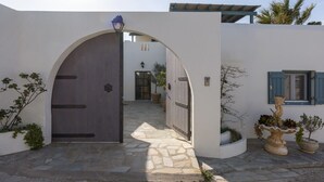 A white building with a large arched entrance, a stone pathway, and potted plants. - Yema House - Naoussa Bay (4666+369 Protorgia, Greece)