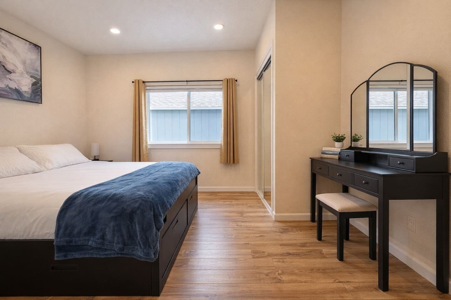 Quarto com cama, escrivaninha, cadeira, espelho e janela com cortinas.