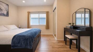 Quarto com cama, escrivaninha, cadeira, espelho e janela com cortinas.