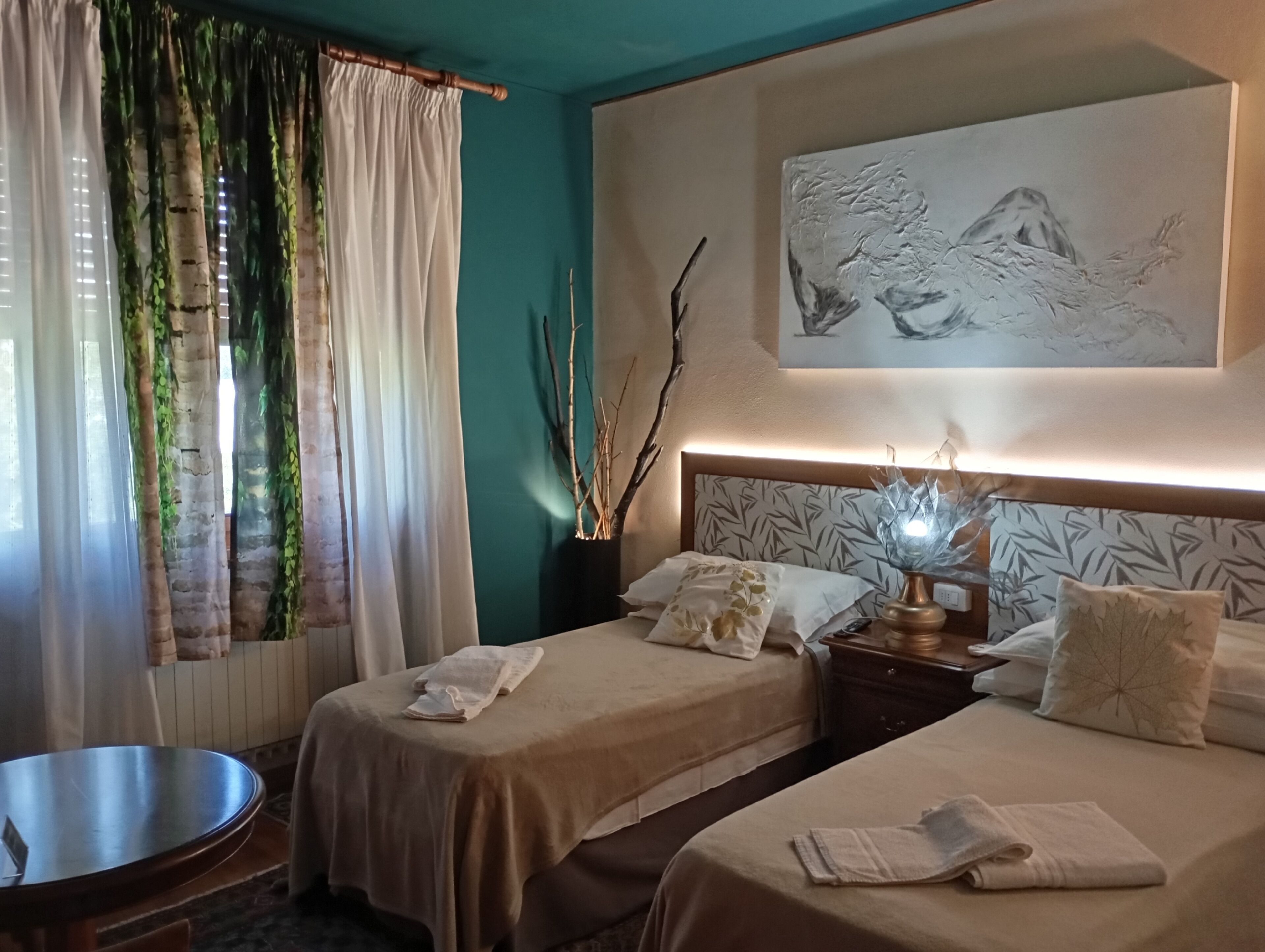 A hotel room with two beds, a dining table, a wall-mounted painting, and a bedside lamp.