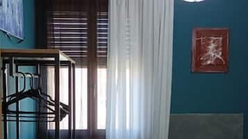 Une pièce comprenant un lit, un bureau, une chaise, un luminaire suspendu et une fenêtre avec des rideaux.