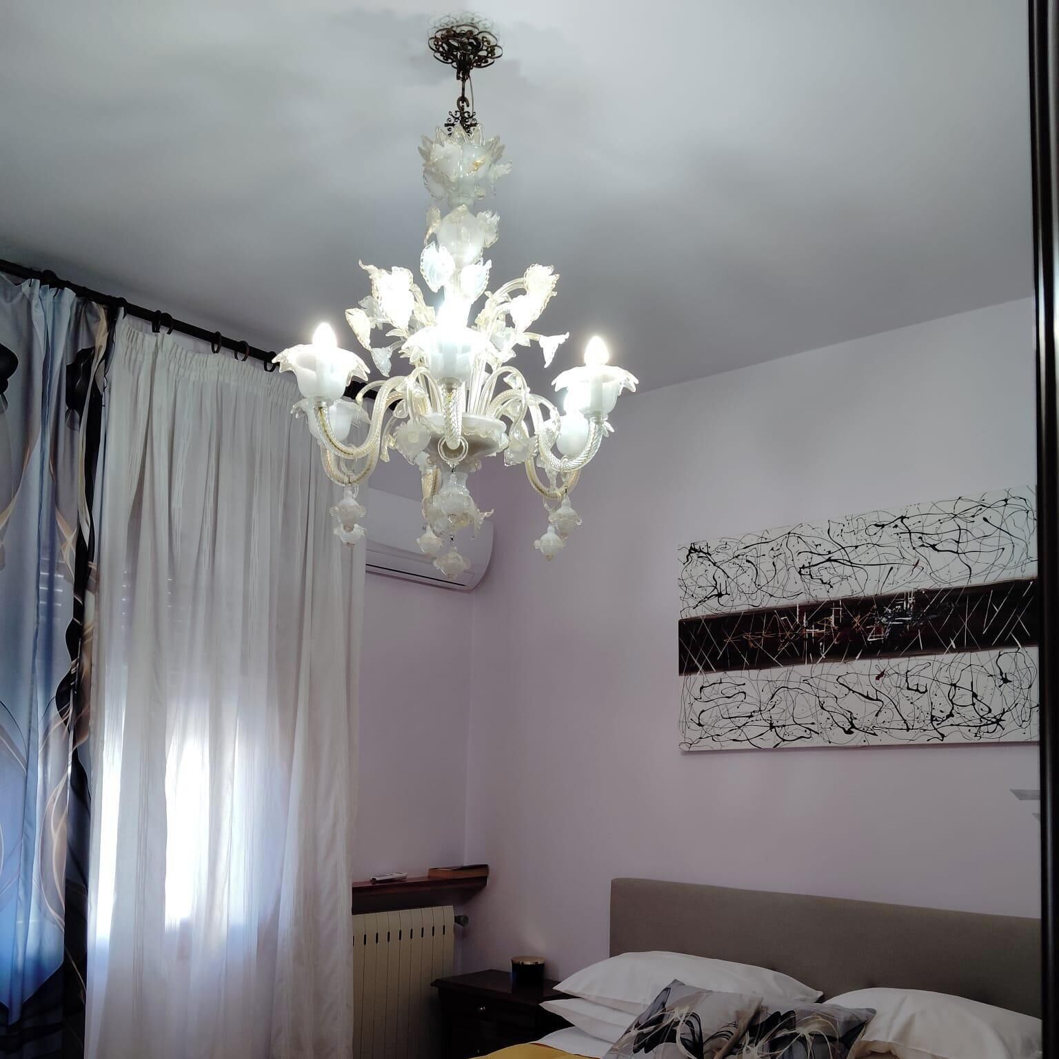 Un dormitorio con candelabro, cama, radiador y un muro con arte abstracto.