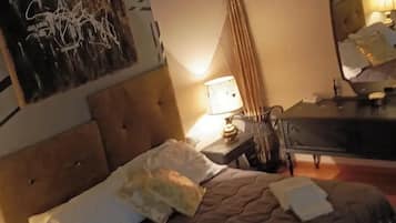 Quarto de hotel com uma cama, mesa de cabeceira, abajur, espelho e um quadro de arte abstrata na parede.