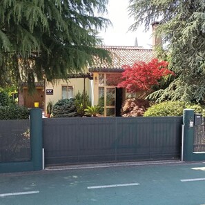 Une propriété privée, fermée par un portail, avec une plaque numérotée, une entrée abritée et une variété de plantes.
