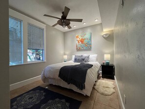 Une chambre à coucher avec un lit, un ventilateur de plafond, un tableau et une table de chevet.