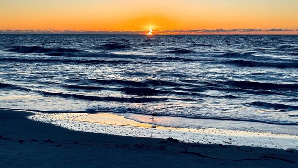 Een strand met golven en een zonsondergang.
