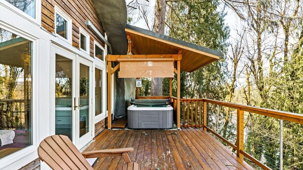 Una terraza de madera con un jacuzzi, sillas de madera y vistas a árboles.