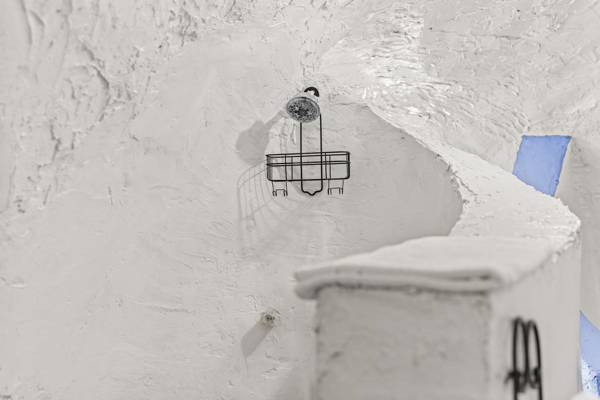 A white textured wall with a metal rack and a small hole.