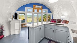 Una cocina con armarios blancos, encimera de mármol y vistas al exterior a través de amplios ventanales.