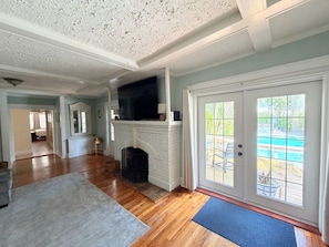 A spacious living room with hardwood floors, a fireplace, and a large sliding glass door leading to an outdoor area. - `Oasis` Historic Beachside Cottage 3/2 (Indian Rocks Beach)